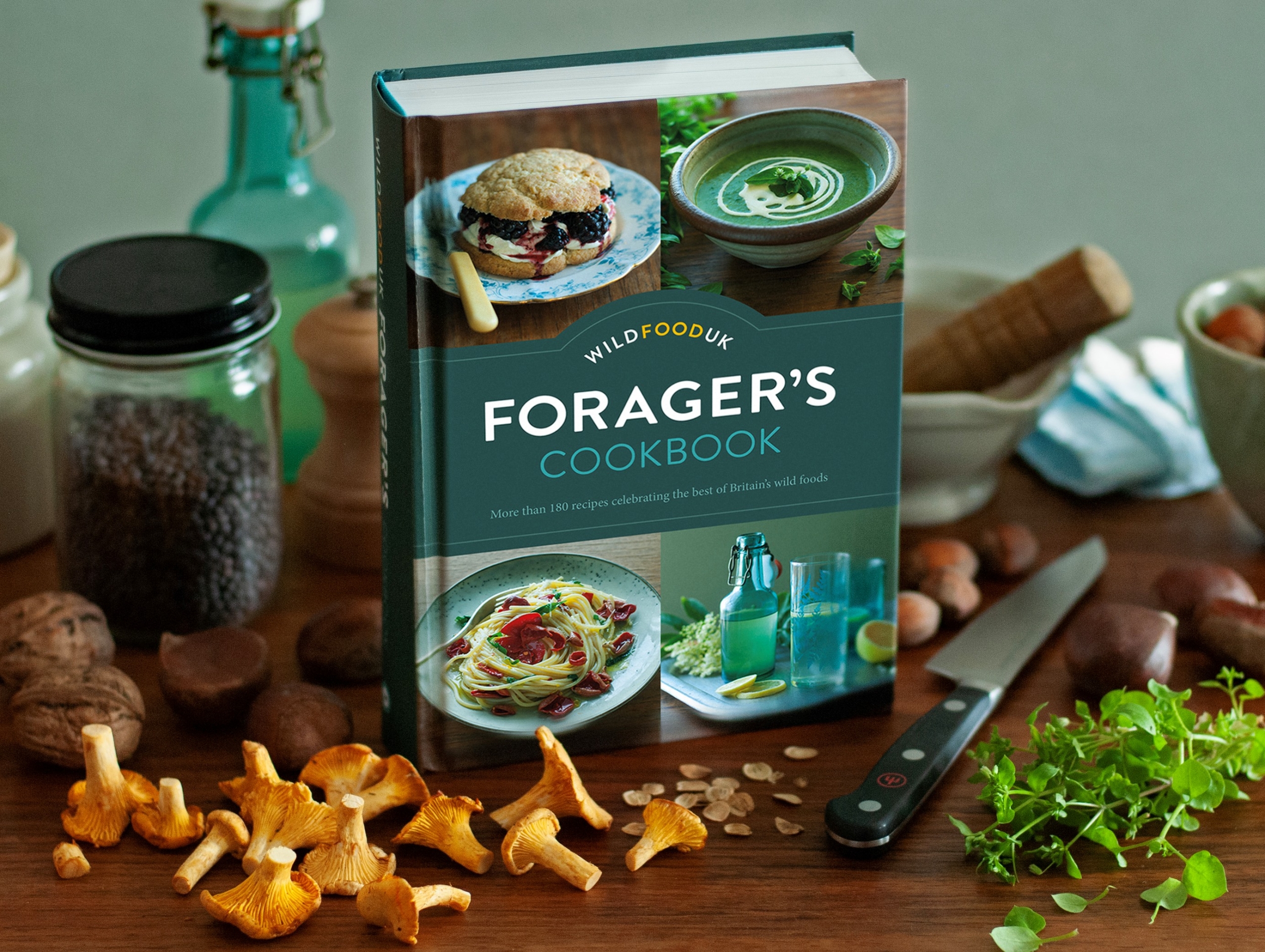 The Wild Food UK Forager's Cookbook on a table surrounded by wild ingredients